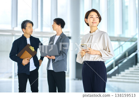 一群人在明亮的辦公室工作，帶著微笑的職業女性手持智慧型手機。 138159513