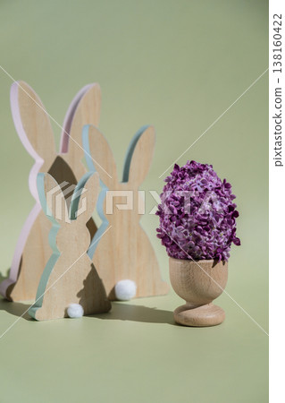 Wooden minimalism low-key bunny decor. Easter egg made of lilac spring flowers in pastel green background. Sustainable holiday minimalistic still life composition. Copy space template for invitation 138160422