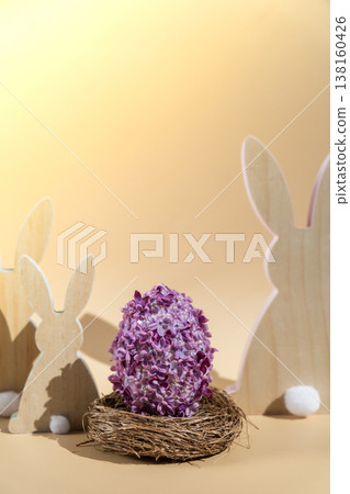 Wooden minimalism low-key bunny decor. Easter egg made of lilac spring flowers in pastel beige background. Sustainable holiday minimalistic still life composition. Copy space template for invitation Wooden minimalism low-key bunny decor. Easter egg made of lilac spring flowers in pastel beige background. Sustainable holiday minimalistic still life composition. Copy space template for invitation 138160426