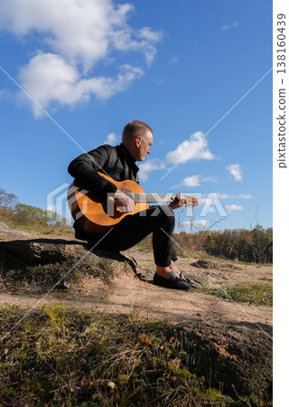 Portrait of smiling caucasian artist plays wooden acoustic guitar in autumnal park. Young songwriter plays string musical instrument hobby outside in nature fall time. Audio music healing Portrait of smiling caucasian artist plays wooden acoustic guitar in autumnal park. Young songwriter plays string musical instrument hobby outside in nature fall time. Audio music healing 138160439