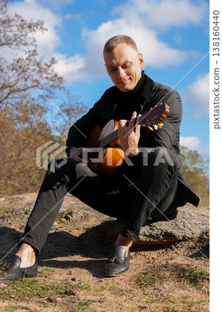 Portrait of smiling caucasian artist plays wooden acoustic guitar in autumnal park. Young songwriter plays string musical instrument hobby outside in nature fall time. Audio music healing Portrait of smiling caucasian artist plays wooden acoustic guitar in autumnal park. Young songwriter plays string musical instrument hobby outside in nature fall time. Audio music healing 138160440