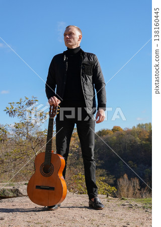 Portrait of smiling caucasian artist plays wooden acoustic guitar in autumnal park. Young songwriter plays string musical instrument hobby outside in nature fall time. Audio music healing 138160445