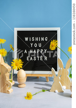 WISHING YOU A HAPPY EASTER text on letter board with bunny wooden figures and fresh flowers. Easter composition content still life. Christian symbols of spring 138160450