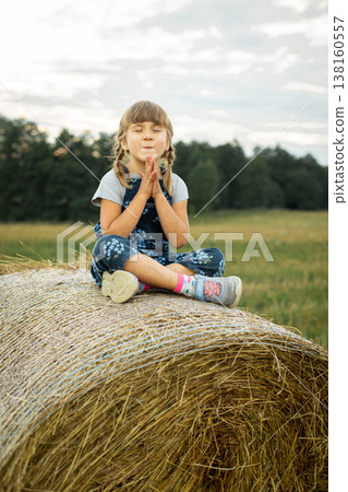 Cheerful little girl sitting on a haystack with her eyes closed Cheerful little girl sitting on a haystack with her eyes closed 138160557