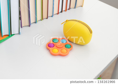 Colorful pop it toy and yellow pouch on desk with books in background 138161966