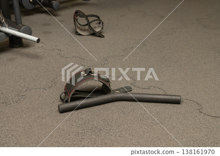 Gym equipment on rubber floor: handlebar, adjustable dumbbell, safety strap Gym equipment on rubber floor: handlebar, adjustable dumbbell, safety strap 138161970