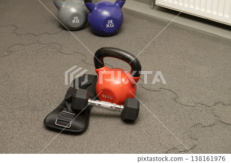 Home gym equipment with red kettlebell, dumbbell, and ankle weights on floor Home gym equipment with red kettlebell, dumbbell, and ankle weights on floor 138161976