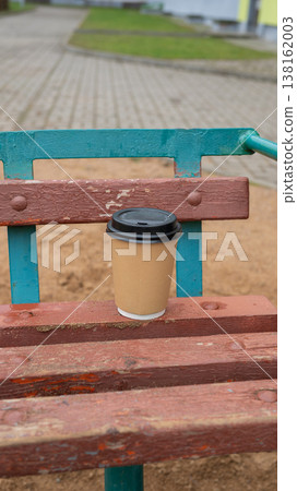 Disposable coffee cup on weathered wooden park bench in urban setting Disposable coffee cup on weathered wooden park bench in urban setting 138162003