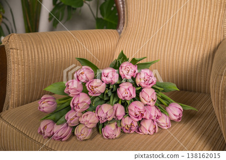Bouquet of pink tulips on a beige armchair with greenery in the background 138162015