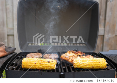Grilling barbecue: corn and meat on outdoor gas grill in backyard setting Grilling barbecue: corn and meat on outdoor gas grill in backyard setting 138162019
