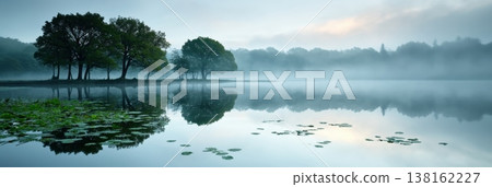 Panoramic misty lake reflection with distant trees and lily pads for serene panoramic background and wallpaper design 138162227