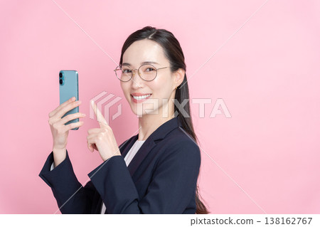 A smiling businesswoman using her smartphone (pink background, spring) 138162767