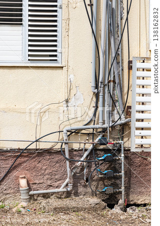 Old water supply pipes with valves and meters mounted on exterior wall of residential building. Urban infrastructure and water distribution system concept Old water supply pipes with valves and meters mounted on exterior wall of residential building. Urban infrastructure and water distribution system concept 138162832