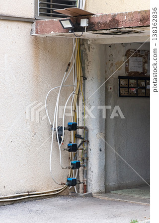 Old water supply pipes with valves and meters mounted on exterior wall of residential building. Urban infrastructure and water distribution system concept Old water supply pipes with valves and meters mounted on exterior wall of residential building. Urban infrastructure and water distribution system concept 138162836