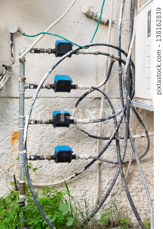 Old water supply pipes with valves and meters mounted on exterior wall of residential building. Urban infrastructure and water distribution system concept 138162839