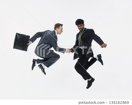 Two businessmen jumping in air while shaking hands on white background. Two businessmen jumping in air while shaking hands on white background. 138162869