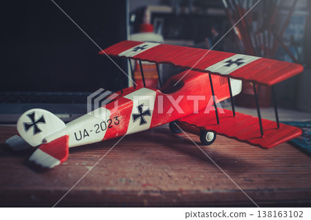 Horizontal side-angle view of a handcrafted red and white wooden triplane model with a propeller, resting on a wooden workbench in a workshop. Horizontal side-angle view of a handcrafted red and white wooden triplane model with a propeller, resting on a wooden workbench in a workshop. 138163102