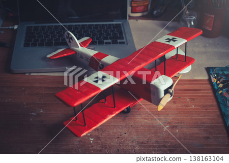 Horizontal high-angle view of a handcrafted red and white wooden triplane model with a propeller, positioned on a workbench in a workshop Horizontal high-angle view of a handcrafted red and white wooden triplane model with a propeller, positioned on a workbench in a workshop 138163104