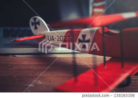 Horizontal close-up view of the tail section of a handcrafted red and white wooden triplane model, resting on a desk in a workshop. Horizontal close-up view of the tail section of a handcrafted red and white wooden triplane model, resting on a desk in a workshop. 138163106