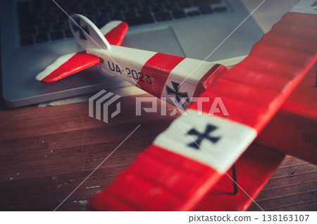 Horizontal close-up view of the tail section of a handcrafted red and white wooden triplane model, resting on a desk in a workshop. Horizontal close-up view of the tail section of a handcrafted red and white wooden triplane model, resting on a desk in a workshop. 138163107