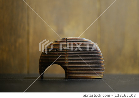 Horizontal close-up of a stylized wooden elephant sculpture with a unique burnt striped texture, standing on a dark surface against a blurred background. Horizontal close-up of a stylized wooden elephant sculpture with a unique burnt striped texture, standing on a dark surface against a blurred background. 138163108