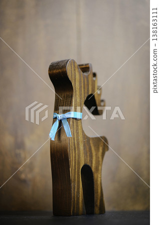 Vertical close-up of a handcrafted wooden reindeer sculpture with a dark brown finish and a small blue ribbon tied around its neck, set against a blurred wooden background. 138163111