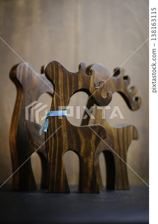 Vertical view of a group of three handcrafted wooden reindeer sculptures of various sizes, with the front one decorated with a thin blue ribbon. Vertical view of a group of three handcrafted wooden reindeer sculptures of various sizes, with the front one decorated with a thin blue ribbon. 138163115