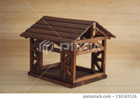 Horizontal three-quarter view of a handcrafted dark wood bird feeder or decorative miniature house, featuring a gabled roof and open timber-frame construction. Horizontal three-quarter view of a handcrafted dark wood bird feeder or decorative miniature house, featuring a gabled roof and open timber-frame construction. 138163126