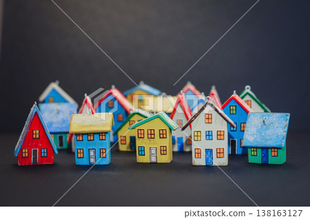 Horizontal view of a colorful collection of handcrafted miniature wooden houses, each uniquely painted with vibrant colors and snowy roofs, arranged on a dark surface. 138163127