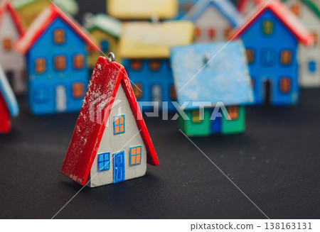 Horizontal view of a colorful collection of handcrafted miniature wooden houses, each uniquely painted with vibrant colors and snowy roofs, arranged on a dark surface. 138163131