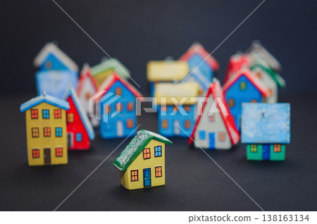 Horizontal view of a colorful collection of handcrafted miniature wooden houses, each uniquely painted with vibrant colors and snowy roofs, arranged on a dark surface. 138163134