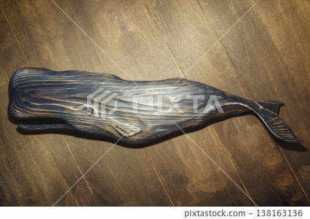 Horizontal high-angle view of a large handcrafted dark wooden sperm whale sculpture with a textured, burnt finish, mounted on a wood plank wall. 138163136