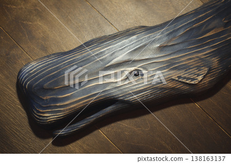 Horizontal close-up of a handcrafted wooden sperm whale head with a burnt texture and a realistic glass eye, mounted on a rustic wood plank wall. 138163137