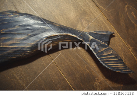 Horizontal close-up of a handcrafted wooden sperm whale tail with a deep burnt texture, showcasing the intricate carved fins against a dark wood plank background. 138163138