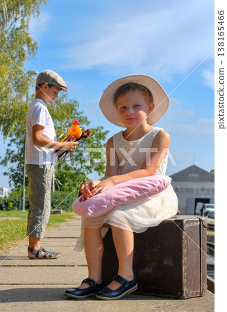 A cute and sweet little girl and boy on a train station platform. A charming pair of siblings at the train station. The concept of travel, vacations, and a carefree childhood. Retro and vintage feel. A cute and sweet little girl and boy on a train station platform. A charming pair of siblings at the train station. The concept of travel, vacations, and a carefree childhood. Retro and vintage feel. 138165466