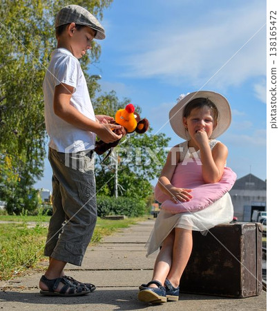 Little children - girl and boy on a railway station, waiting for the train with vintage suitcase. Traveling, holiday and chilhood concept. Travel insurance concept. Travel, tourism, summer vacation 138165472