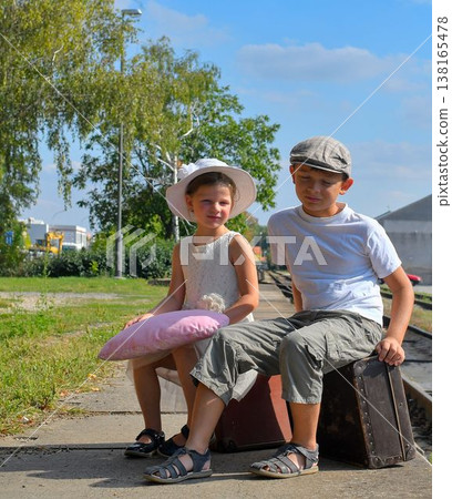 Adorable siblings on a train platform. A little girl and boy travel for vacation. The concept of journey, holidays, and carefree childhood. Vintage and retro feel. Adorable siblings on a train platform. A little girl and boy travel for vacation. The concept of journey, holidays, and carefree childhood. Vintage and retro feel. 138165478