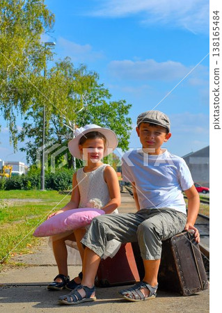 Cute siblings on a train platform. A little girl and boy are traveling on vacation. The concept of travel, holidays, and a carefree childhood. Vintage and retro spirit. 138165484