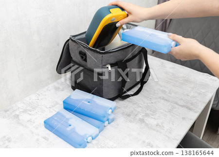 Person hands packing lunchbox food container and ice packs into insulated cooler bag on table ready for picnic camping trip or outdoor activity 138165644