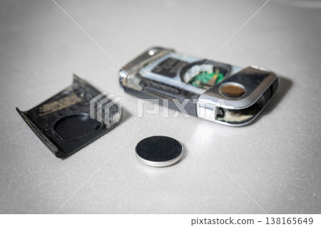 Disassembled car key fob showing internal circuit board and removed button cell battery on light textured surface, illustrating process of battery replacement Disassembled car key fob showing internal circuit board and removed button cell battery on light textured surface, illustrating process of battery replacement 138165649