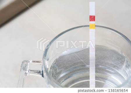 Water test strip immersion in clear glass of water displaying chemical reaction color changes measurement of water parameters for quality analysis of drinking water for safety and health purposes 138165654