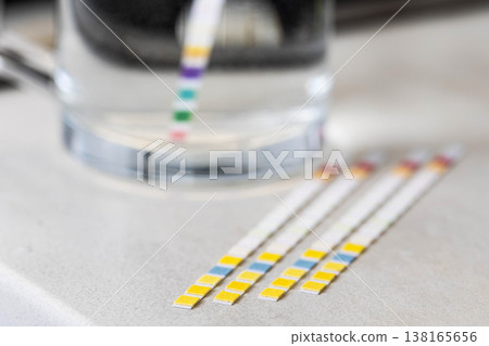 Water quality test strips displaying chemical reaction with clear liquid in glass beaker, indicating various parameter measurements for purity and safety analysis 138165656