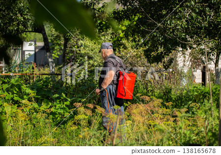 An elderly man with a red sprayer treats plants with ammonia to protect them from diseases and pests at his dacha. Copy space for text, industry An elderly man with a red sprayer treats plants with ammonia to protect them from diseases and pests at his dacha. Copy space for text, industry 138165678
