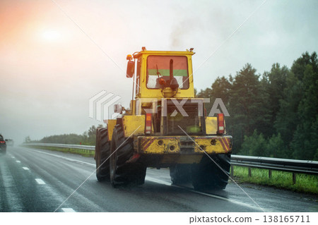 Yellow heavy construction machine moving on wet asphalt road during rain, poor visibility conditions, danger of slippery road surface. Copy space for text Yellow heavy construction machine moving on wet asphalt road during rain, poor visibility conditions, danger of slippery road surface. Copy space for text 138165711