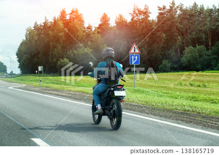 Person riding motorcycle on asphalt highway alongside green forest, wide grass field under bright summer sky, journey on road. Copy space for text Person riding motorcycle on asphalt highway alongside green forest, wide grass field under bright summer sky, journey on road. Copy space for text 138165719