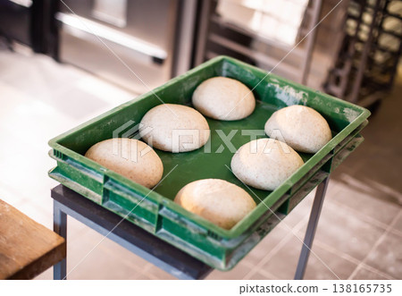 Unbaked dough balls arranged in green plastic proofing crate on metal stand within commercial bakery or kitchen setting highlighting food preparation for artisan bread production Unbaked dough balls arranged in green plastic proofing crate on metal stand within commercial bakery or kitchen setting highlighting food preparation for artisan bread production 138165735