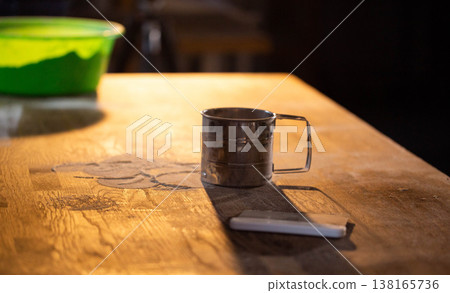 Metal flour sifter on rustic wooden kitchen table, powdery flour dust scattered. Baking preparation tool illuminated by warm light, casting long shadow. Metal flour sifter on rustic wooden kitchen table, powdery flour dust scattered. Baking preparation tool illuminated by warm light, casting long shadow. 138165736