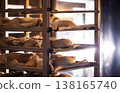 Rising bread dough in linen cloths on multiple shelves of industrial rack at artisan bakery, preparing for traditional baking process 138165740