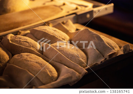 Unbaked bread dough loaves arranged in fabric-lined proofing baskets ready for oven baking in a traditional bread making factory setting Unbaked bread dough loaves arranged in fabric-lined proofing baskets ready for oven baking in a traditional bread making factory setting 138165741