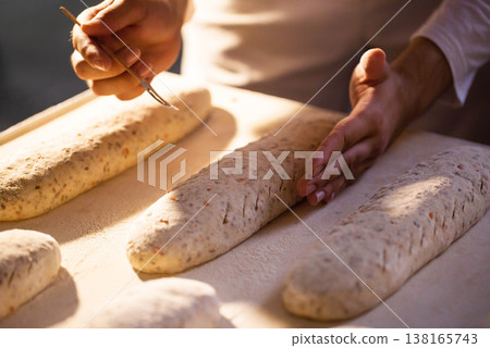 Baker hands scoring raw bread dough with fork tool, preparation of artisanal bakery product before baking, traditional manual bread making process 138165743